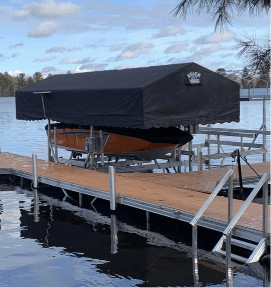 Boat covered by black canopy on a wooden dock by a lake, under partly cloudy sky.