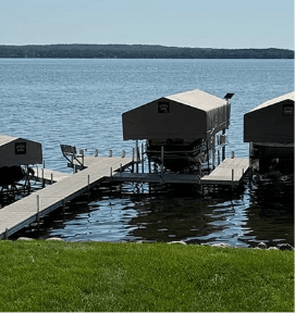 Lakefront view with two docked boats under canopies, wooden piers extending over calm water, and green grass in the foreground.