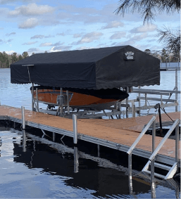 Boat dock with covered lift on a lake under a partly cloudy sky, surrounded by trees and calm water.