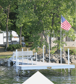 American flag on lakeside dock with trees and a house in the background, ideal summer lake setting.