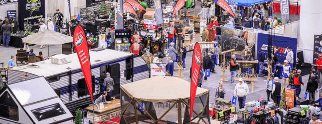 Camping and outdoor gear expo with booths, RVs, and attendees exploring the latest products, banners, and displays.