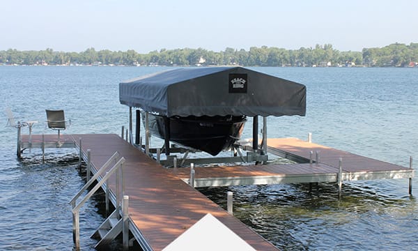 Covered boat on a lake dock surrounded by calm water and distant trees under a clear blue sky.