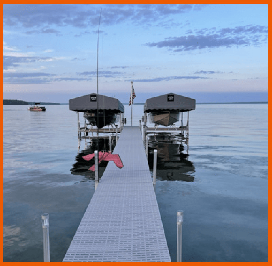 Dock with boats on a lake at sunset, calm water reflecting colorful sky, American flag in the center.