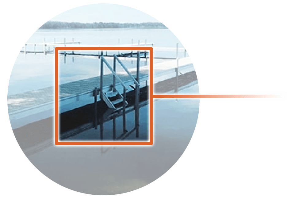 Close-up of dock ladder over water with staircase reflection; calm lakeside scene in background.