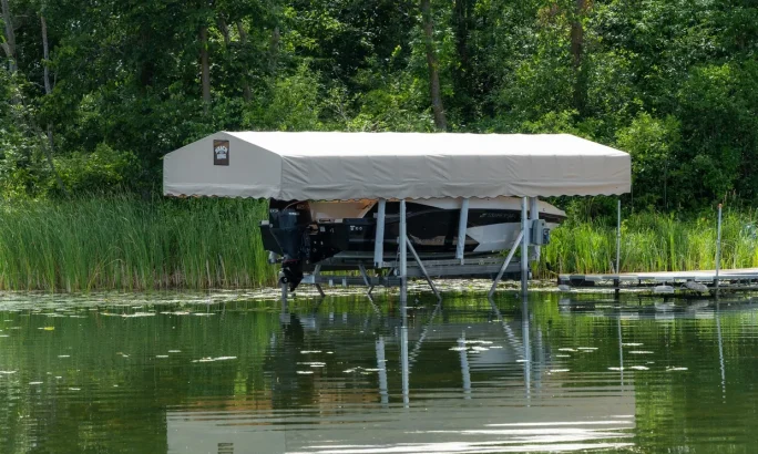 Boat lift with canopy on calm water surrounded by greenery