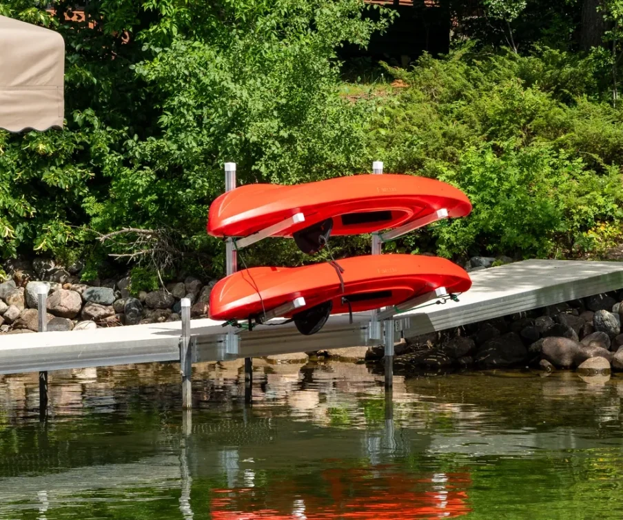 Two red kayaks on a dock near a lush green shoreline